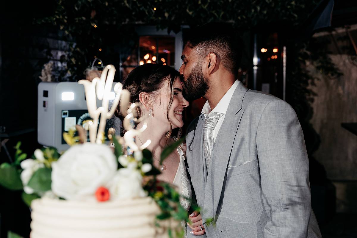 Le marié dépose un baiser sur le front de la mariée pendant la présentation du wedding cake