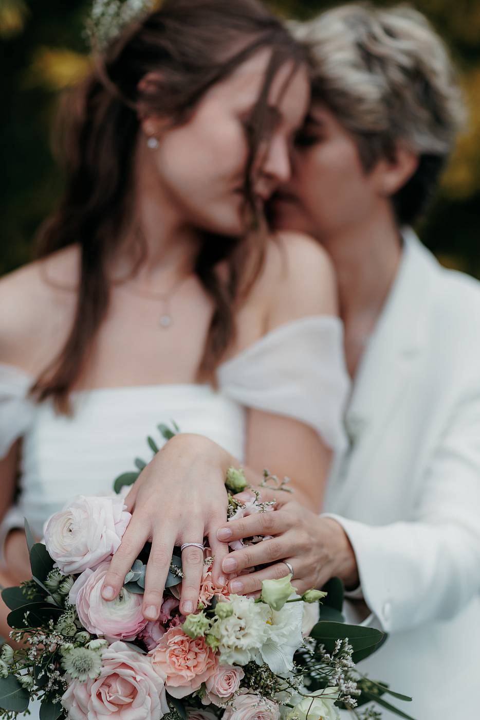 Gros plan sur les alliances et le bouquet des mariées entrain de partager un moment de tendresse