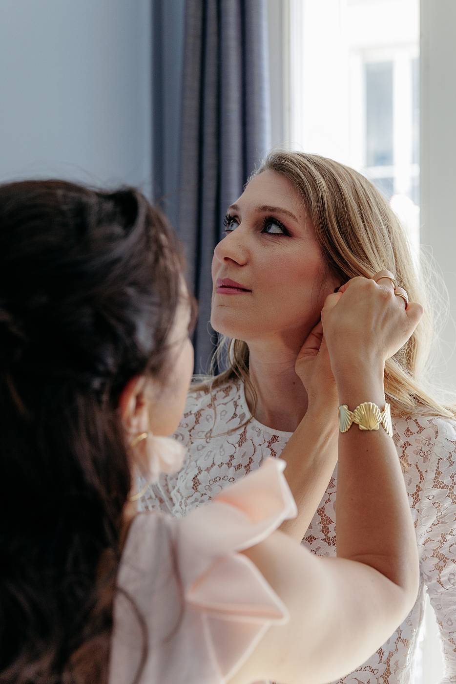 Gros plan sur l'amie de la mariée qui l'aide à accrocher ses boucles d'oreilles