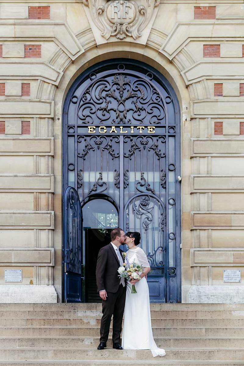 Les mariés s'embrassent devant l'entrée de la mairie de Versailles.