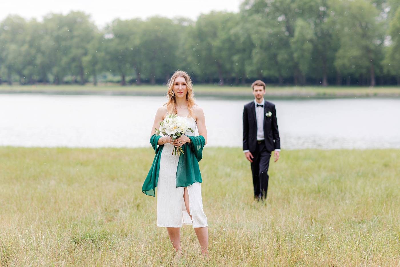 La mariée pose avec son bouquet tandis que le marié la rejoint