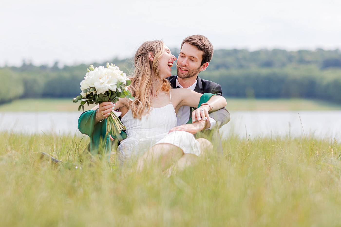 Les mariés, assis dans les hautes herbes, s'amusent près de la pièce d'eau des Suisses