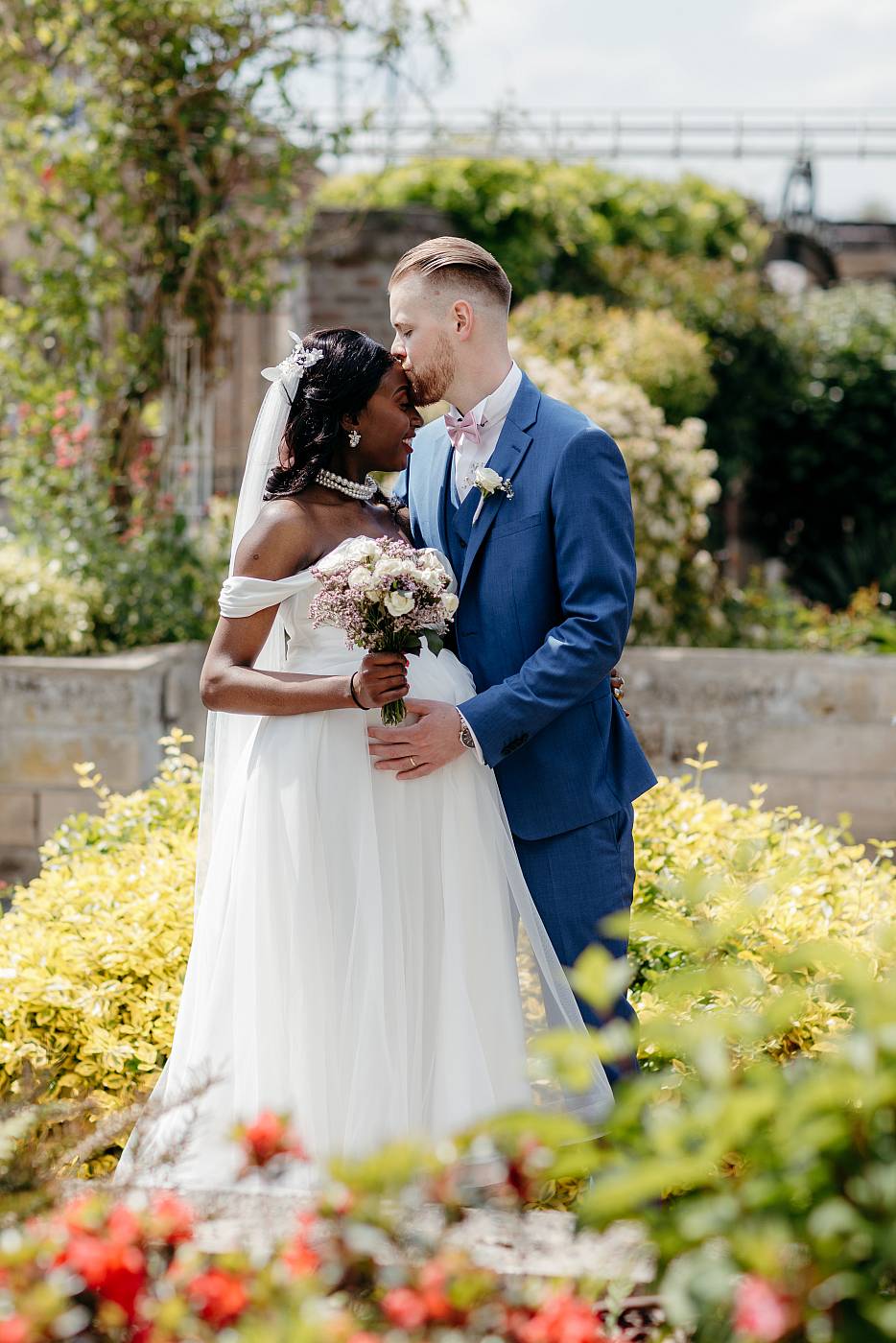 Baiser sur le front de la mariée entouré de fleurs colorées