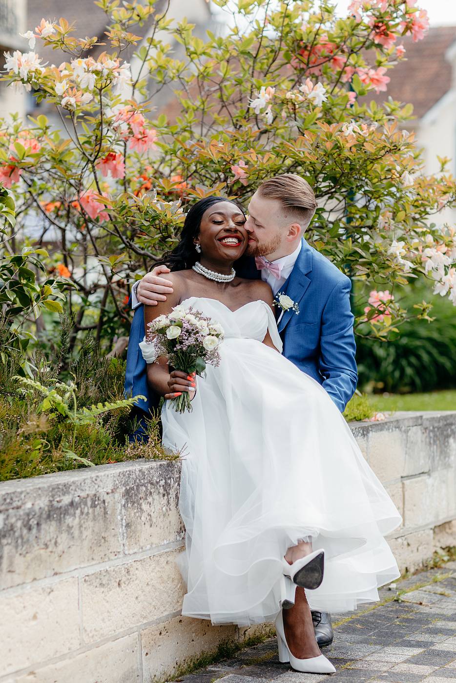 Baiser sur la joue de la mariée dans un décor fleuri dans le parc de la mairie de Plaisir