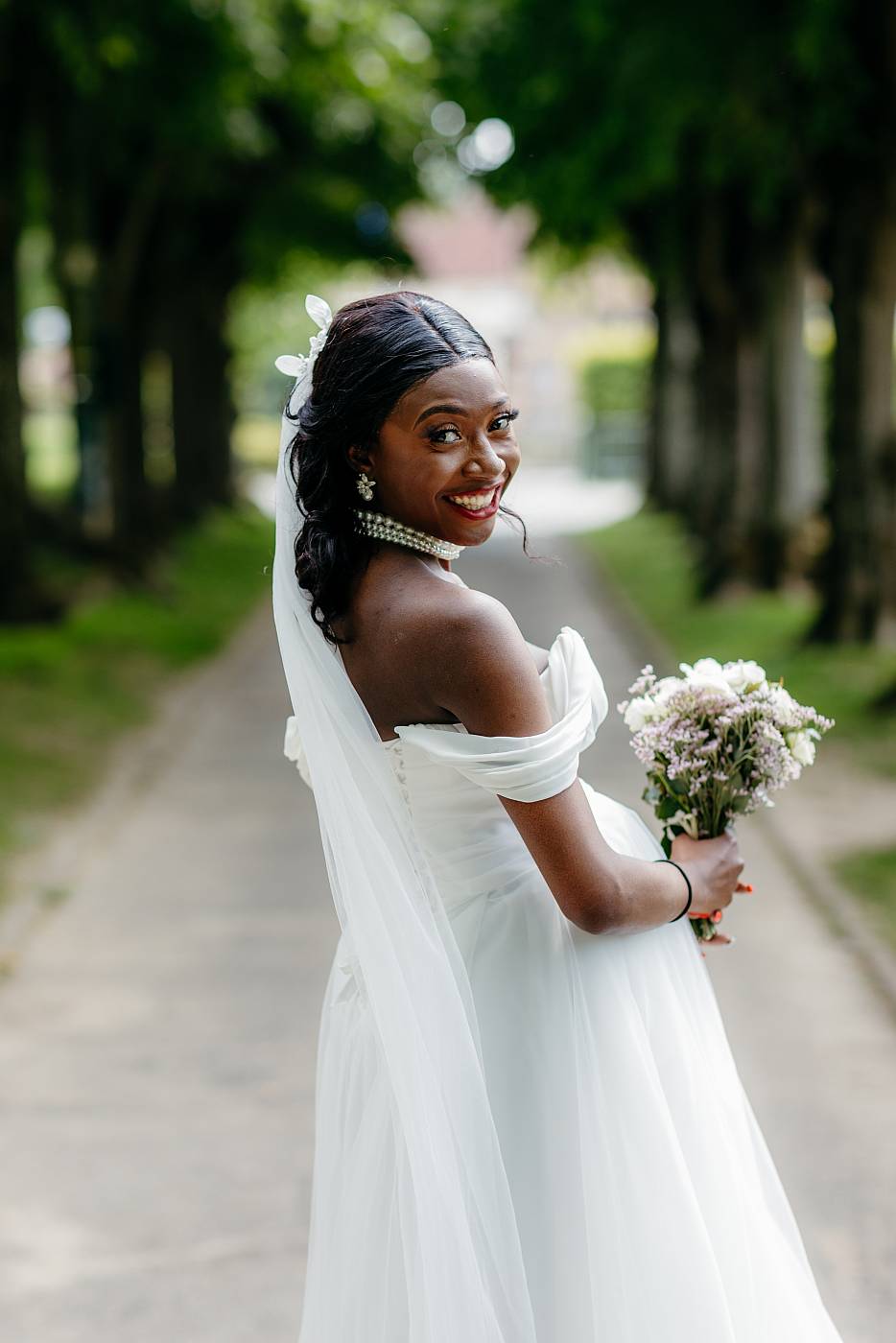 La mariée et son bouquet avec les allées d'arbres en perspective