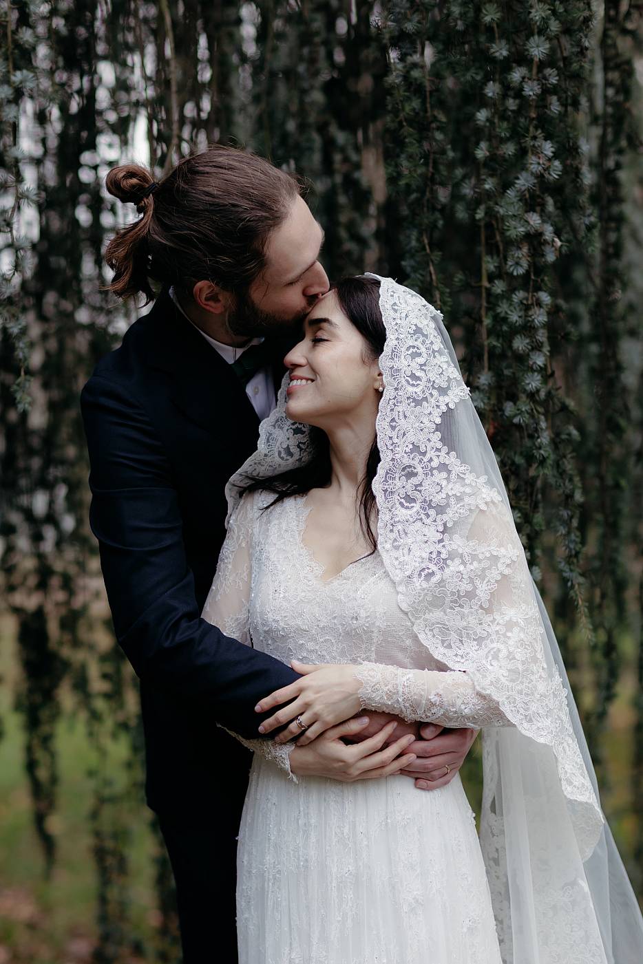 Baiser sur le front de la mariée sous les branches d'un arbre